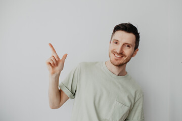 Handsome young man over grey wall with happy face pointing his finger