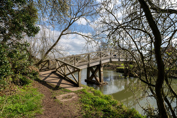 Fototapeta na wymiar A footpath and an old wooden bridge in the forest over the Thames River in England, Cotswolds