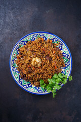 Traditional Uzbek fergana plov with devsira rice and lamb meat served as top view on a handmade painted lagan platter