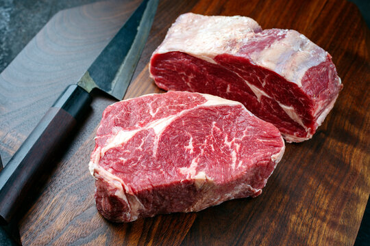 Raw dry aged Angus rib-eye beef steaks offered as close-up on a modern design wooden board
