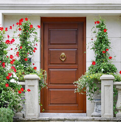 Fototapeta na wymiar Elegant wooden front door surrounded by planters with red amaryllis flowers