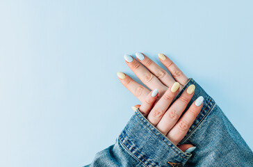 Beautiful groomed female hands with pastel blue and yellow nails on light blue background. Empty place for text.