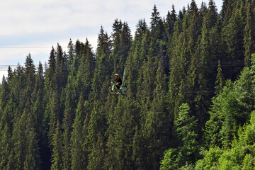 Naklejka premium A young man rides a ride on a bicycle on ropes above the ground. Against the background of green trees