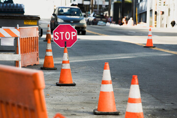 A warning stop sign and orange safety cones in an urban street. Signs of road work.