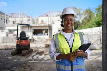 Smiling female engineer, wearing a hard hat, vest, holding a tablet.cute woman with black...