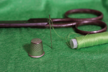 Spool of Green Thread, Thimble and Needle on Green Fabric
