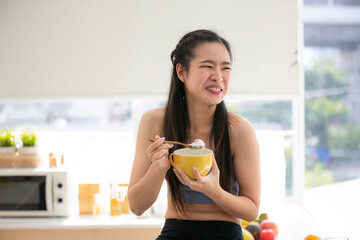 young Asian woman cooking vegetable healthy food and eating or drinking in home kitchen