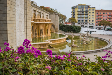 Blurred bougainvillea flowers with Alameda light fountain, statues and building reflected in the...