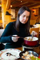 Portrait of cheerful woman eating traditional Swiss cheese fondue
