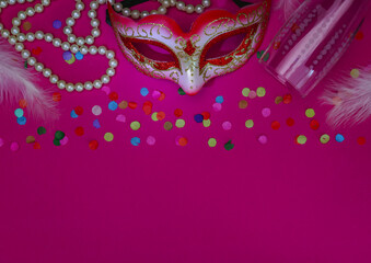 Masquerade mask, white pearl beads, confetti, feathers and an empty champagne glass on a bright pink.