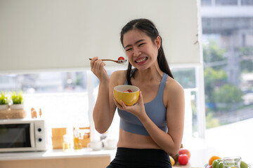 young Asian woman cooking vegetable healthy food and eating or drinking in home kitchen