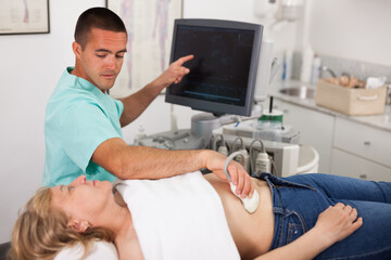 Fototapeta premium Young man sonographer using ultrasonography machine checking female patient in hospital diagnostic room
