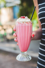 woman holding a tall glass of strawberry milkshake with cream and a cherry