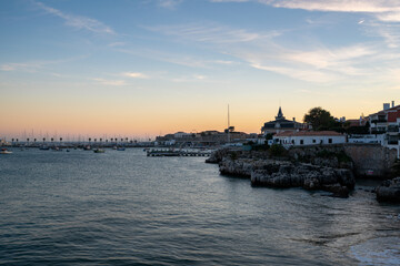 Rainha beach in Cascais at sunset with sail boats on the sea and houses on the coast, in Portugal