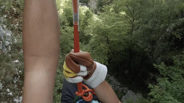 Point of view from a man slacklining on a mountain going through trees. Adrenaline sport - sliding on a zip line in a forest on a summer day.