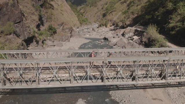 three men walking hiking trekking on metal steel iron bridge spanning across mountain river water in remote rocky valley in Kabayan Benguet Philippines side trucking follow aerial middle of crossing
