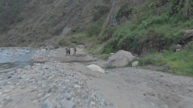 three men standing on the edge of Mountain dirt road vehicle tracks leading out to riverbed opening boulders rocks sand i valley Kabayan Benguet Philippines fast reverse revealing people aerial
