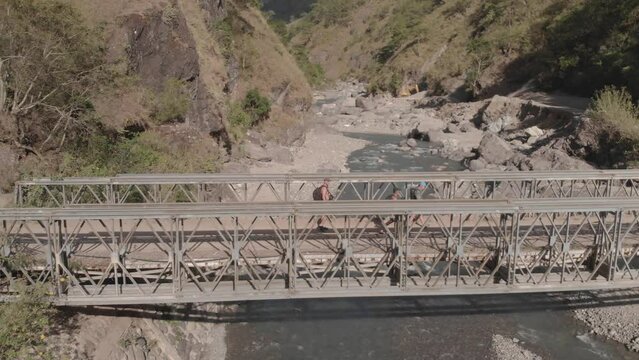three men walking hiking trekking on metal steel iron bridge spanning across mountain river water in remote rocky valley in Kabayan Benguet Philippines side trucking follow aerial angle start crossing