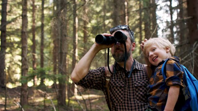 Father with small son looking through binoculars in summer forest.