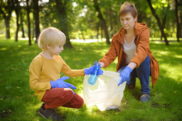 Woman volunteer and little boy picking up the plastic garbage and putting it in biodegradable...