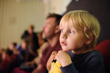 Cute little boy with his father watching cartoon movie in cinema or performance in viewer hall of theatre. Leisure entertainment for family with kids.