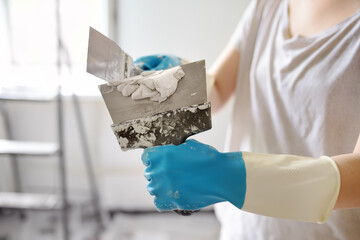 Young female worker preparing putty for the wall repair. Close-up view of spreading plaster on metal spatula. Do it yourself.