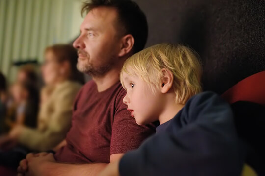 Cute little boy with his father watching cartoon movie in cinema or performance in viewer hall of theatre. Leisure entertainment for family with kids.