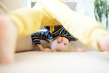 Little boy is standing on own head on sofa at home. Bored lonely child. Difficulties of family with preschool children during working at home. Baby having fun and standing upside down.