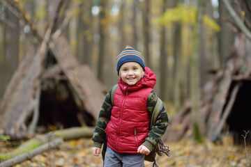 Little boy scout during hiking in autumn forest. Behind the child is teepee hut. Adventure, scouting and hiking tourism for kids.
