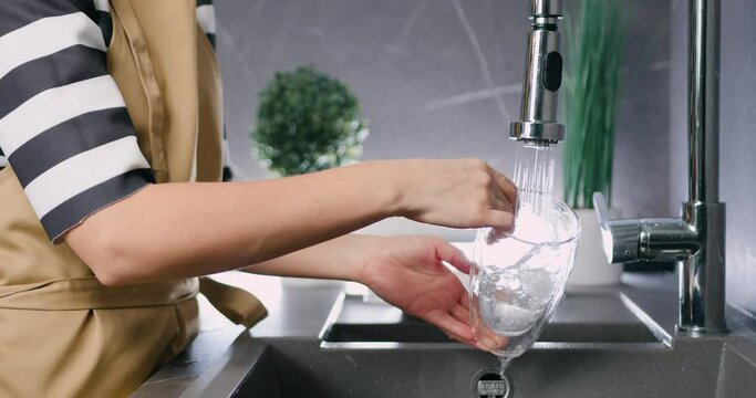 Close up of caucasian female hands washing glass dishes under water jet at modern home kitchen