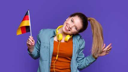Funny Smiling Girl in casual clothes and headphones holds small German flag. Study abroad and...