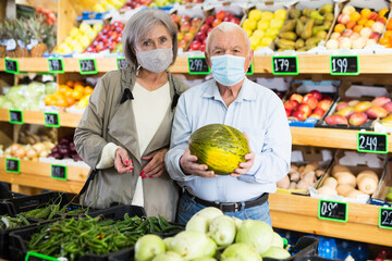 Married couple in protective mask buy ripe watermelon in the supermarket