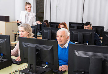 Portrait of modern elderly people working on computers with young female teacher while attending pc...