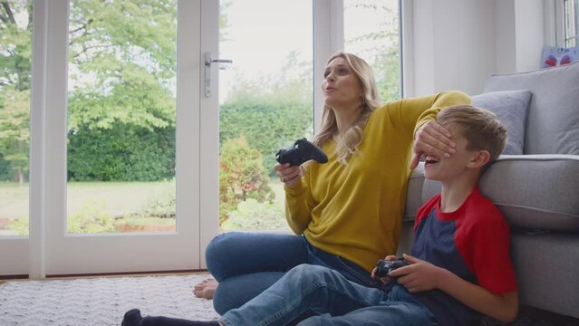 Mother and son at home playing video game together with woman cheating by covering boy's eyes to win - shot in slow motion