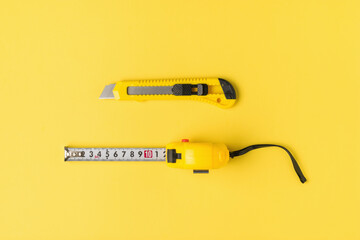 Yellow measuring tape and a yellow stationery knife on a yellow background. Flat lay.