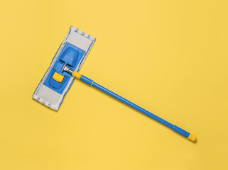 A blue floor mop on a yellow background. The concept of maintaining cleanliness. Flat lay.