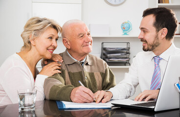 Elderly man and mature woman consulting with employee in social service office