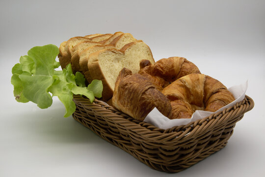 Wicker basket with slices of bread, croissants, white background