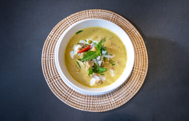 Flatlay Top Table of Green Curry with Chicken garnished on top with pepper, basil was served in white bowl on wicker placemat cream color. Clipping Path.