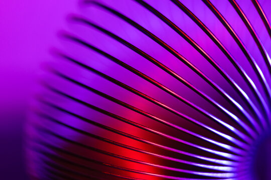 Closeup of coiled metal spring with sufficiently high strength and elastic properties in neon purple and pink light. Macro photo, selective focus.