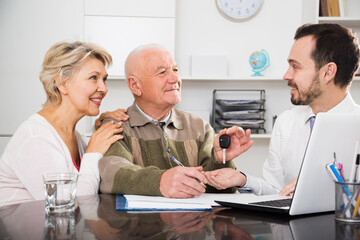 Old man and and woman signing car sale contract at office and hand over keys to manager