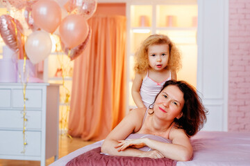 A happy mother and daughter in pink pajamas are lying on the bed in the bedroom. The concept of family, love and care