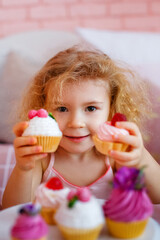 A little curly-haired girl in bed is holding cakes in her hands. Selective focus.