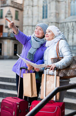 Happy mature ladies travellers with suitcases visiting sights of European city with map