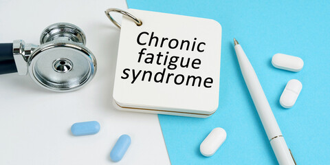 On a white and blue surface are pills, a stethoscope, a pen and a notepad with the inscription Chronic fatigue syndrome