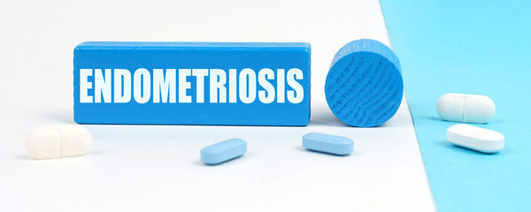 On a white and blue surface are pills, a pen and a wooden sign with the inscription - Endometriosis