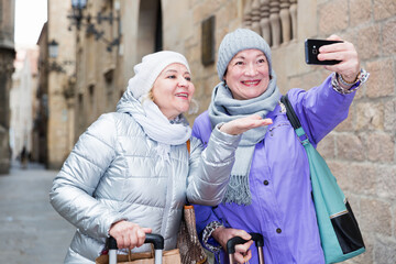 Two smiling senior ladies making selfie outdoors while traveling together