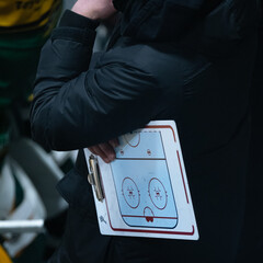 Ice hockey coach holding a flip chart while watcing the game