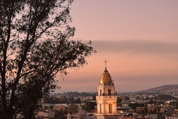 C&uacute;pula iluminada de iglesia colonial al atardecer en paisaje urbano mexicano