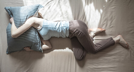 Unslept woman is lying in bed in the morning, covering her head with a pillow. Concept of insomnia, sleep disorders due to anxiety or depression. Top view